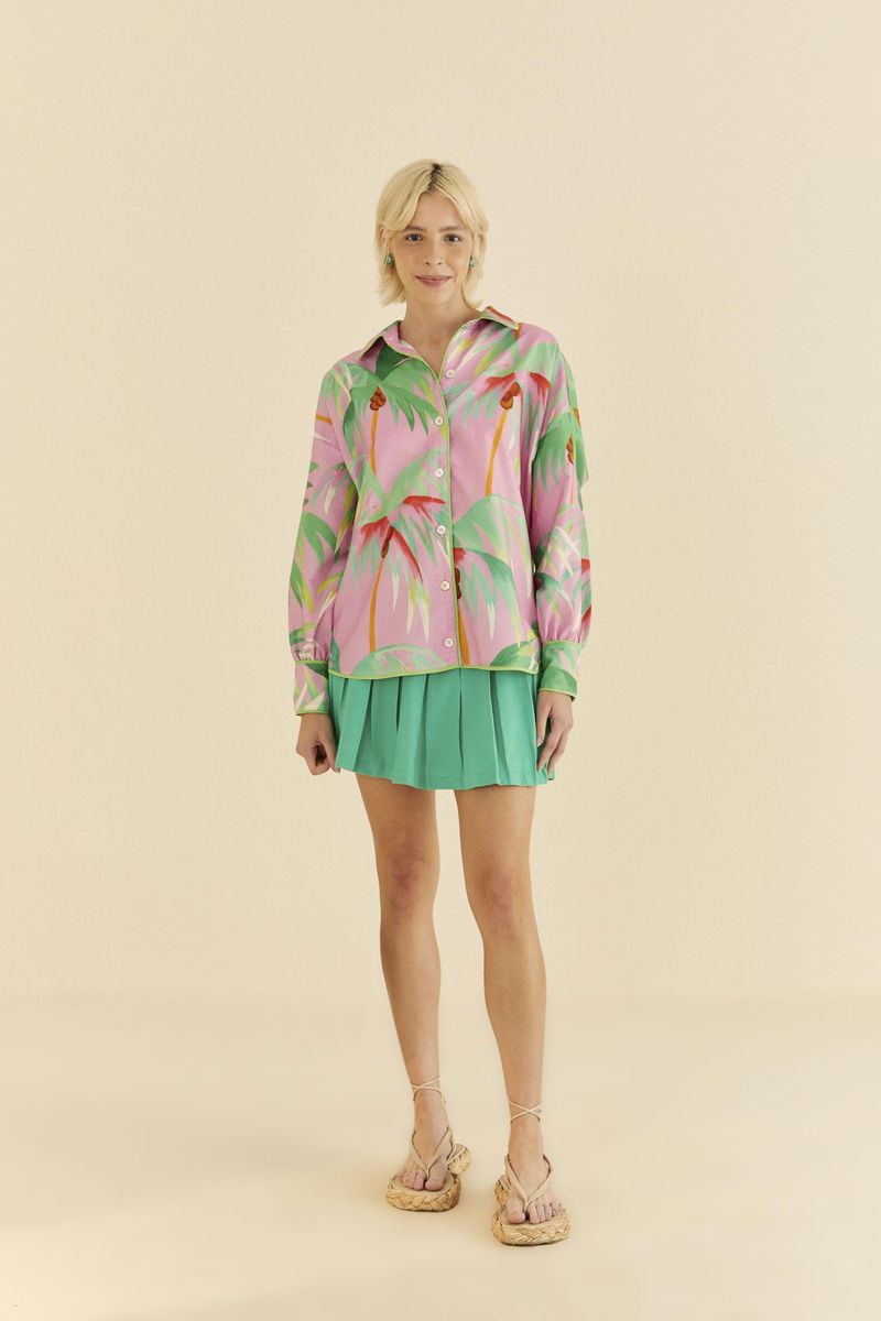 Vista-frontal-de-una-camisa-estampada-con-cocoteros-en-tonos-de-verde-y-rosa-sobre-fondo-rosa-combinada-con-falda-verde.