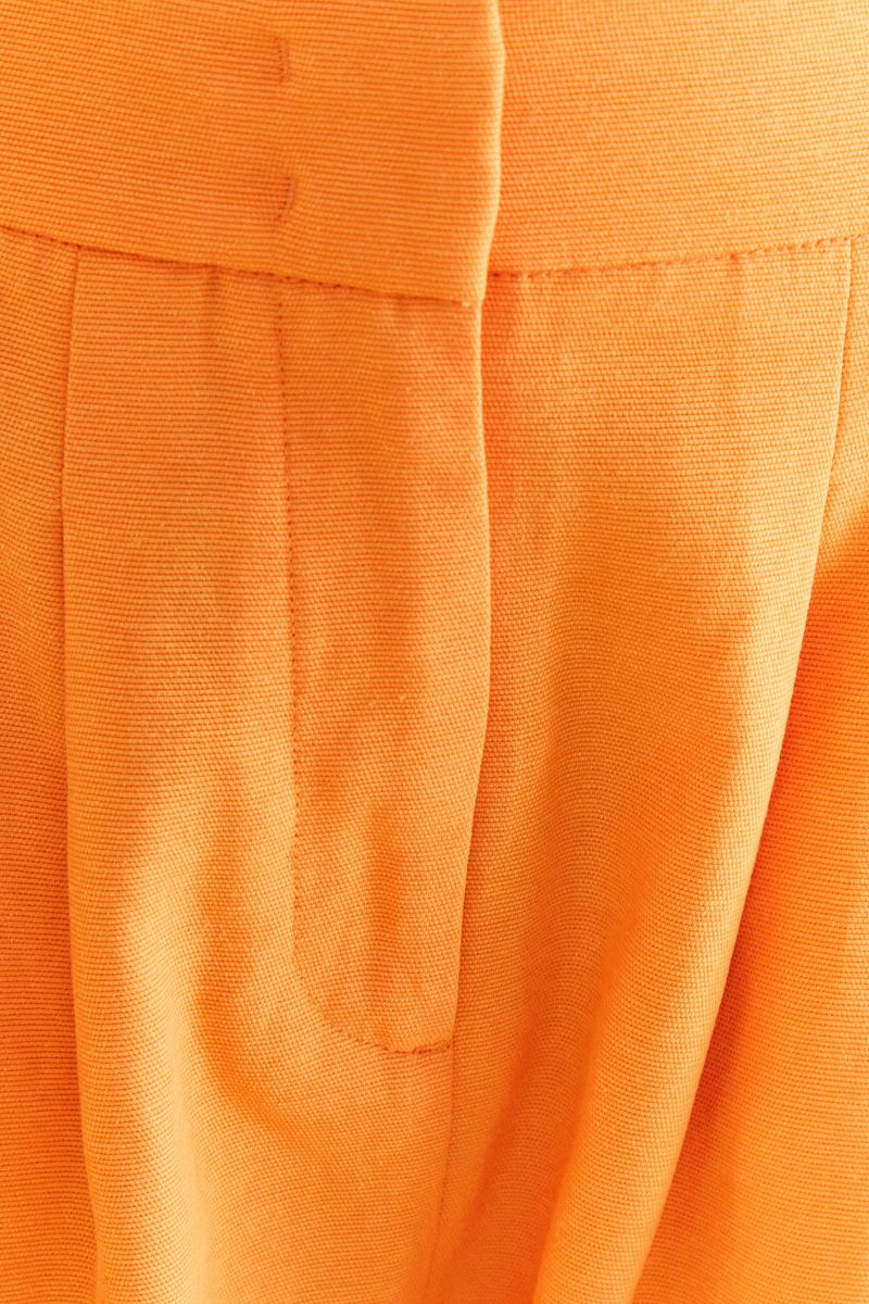 Acercamiento del tejido naranja del pantalón de sastrería mostrando los detalles de las pinzas.