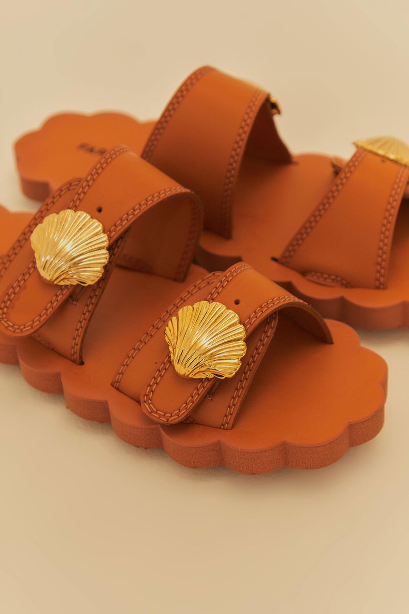 Close-up del detalle de concha dorada en las sandalias caramelo.