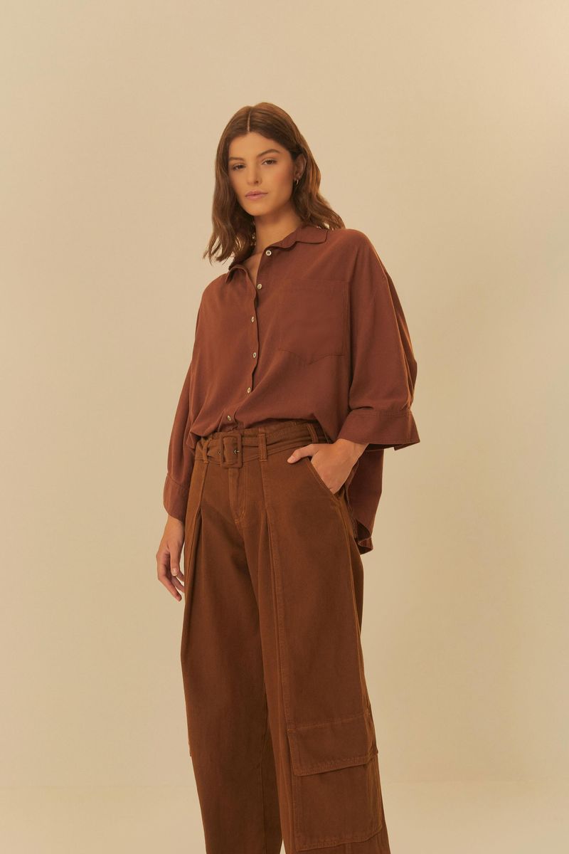 Modelo usando pantalones cargo de sarga marrón con cinturón, combinados con una camisa suelta marrón, sobre un fondo neutro.
