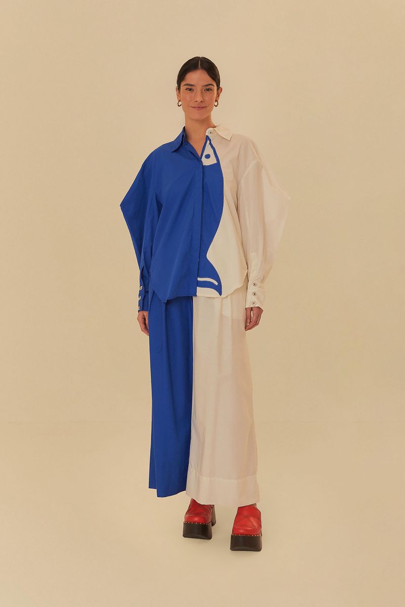 Modelo luciendo pantalón bicolor de sastrería con camisa azul asimétrica.