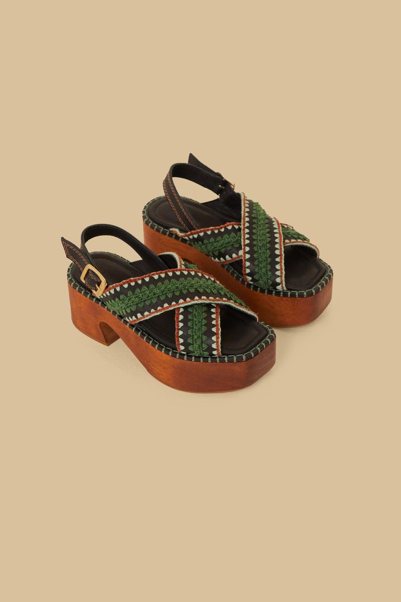 Sandalia estilo clog con correas trenzadas en verde y marrón, vista lateral mostrando la suela de madera.