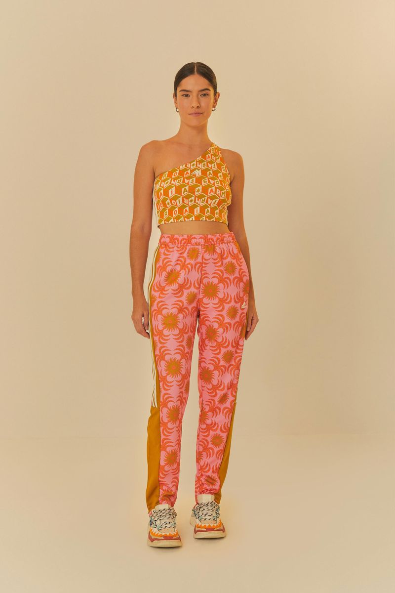 Modelo usando un conjunto vibrante con un top de un solo hombro y pantalón Adidas Palm Flower Rosa, destacando el diseño floral en tonos de rosa y amarillo.