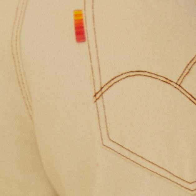Detalle de la costura contrastante y etiqueta multicolor en el bolsillo trasero del pantalón recorte sarga off