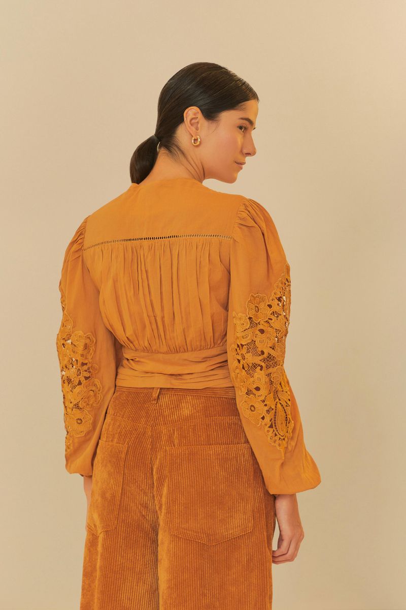 Vista trasera de la blusa romántica bordada, mostrando detalles del diseño y mangas amplias.
