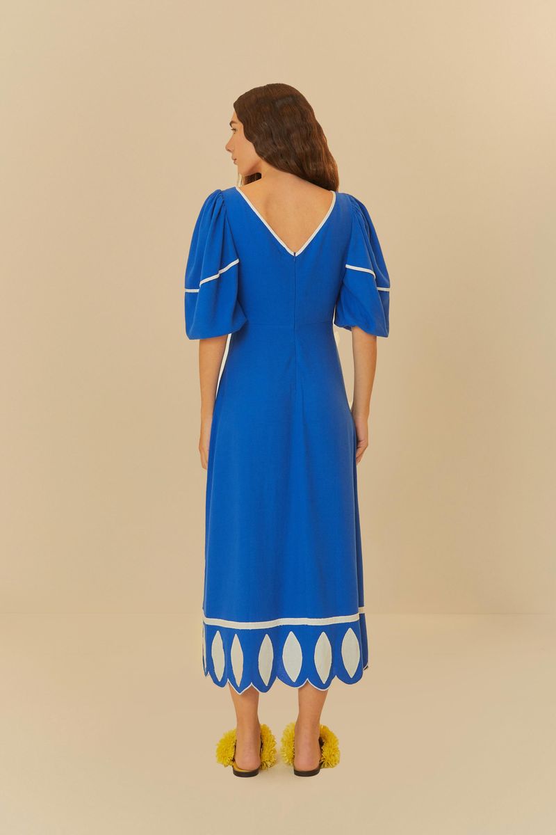 Acercamiento del escote en V y mangas abultadas del vestido azul con bordados blancos.