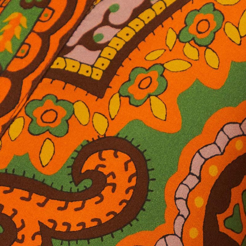 Detalle del estampado del vestido, mostrando elementos decorativos en tonos de verde, naranja y rosa.