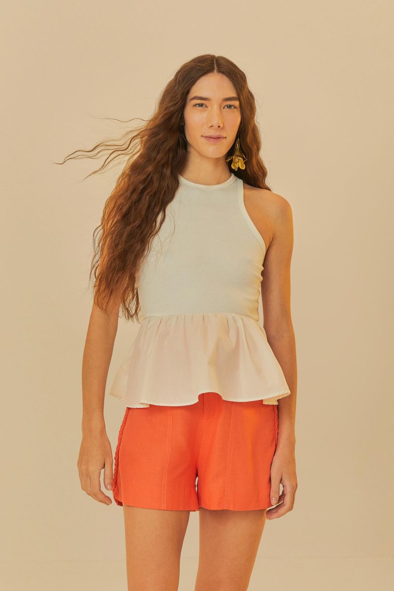Modelo usando un short naranja con detalle de trenzado lateral, combinado con una blusa blanca.