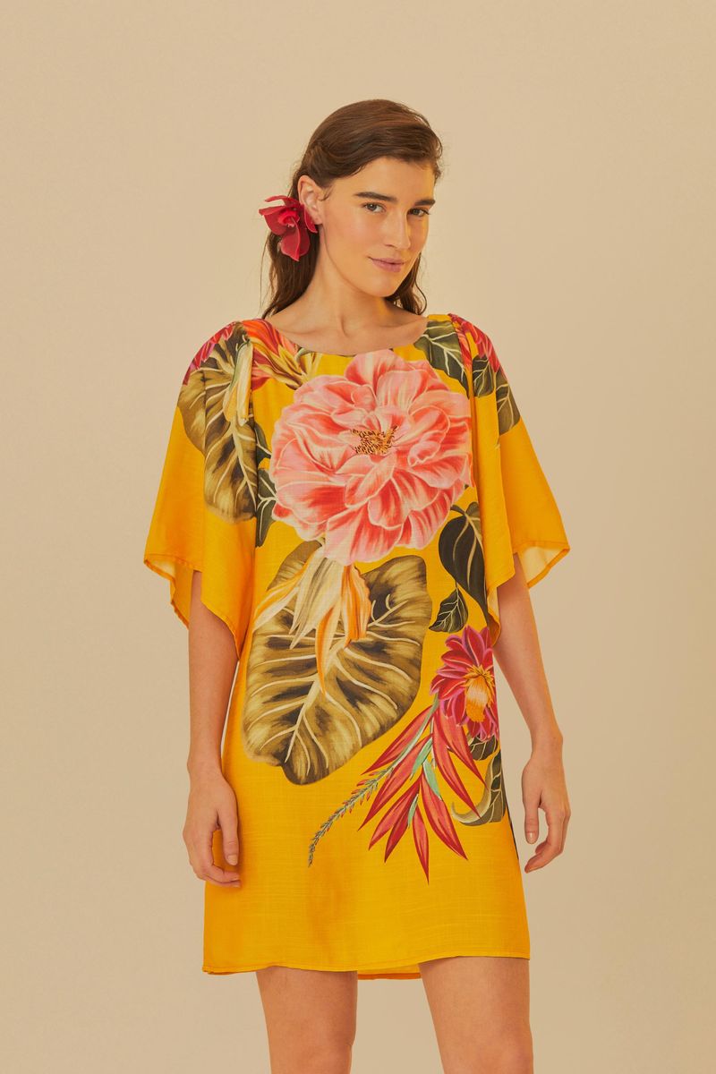 Vestido corto con diseño floral vibrante sobre fondo amarillo, con mangas anchas y escote redondo.