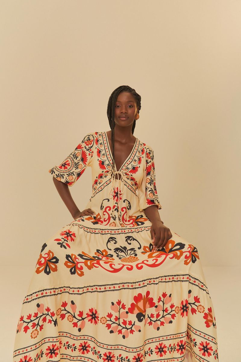 Imagen de una modelo sentada usando un vestido largo estampado con motivos florales y geométricos, mostrando detalles del corsé y mangas.