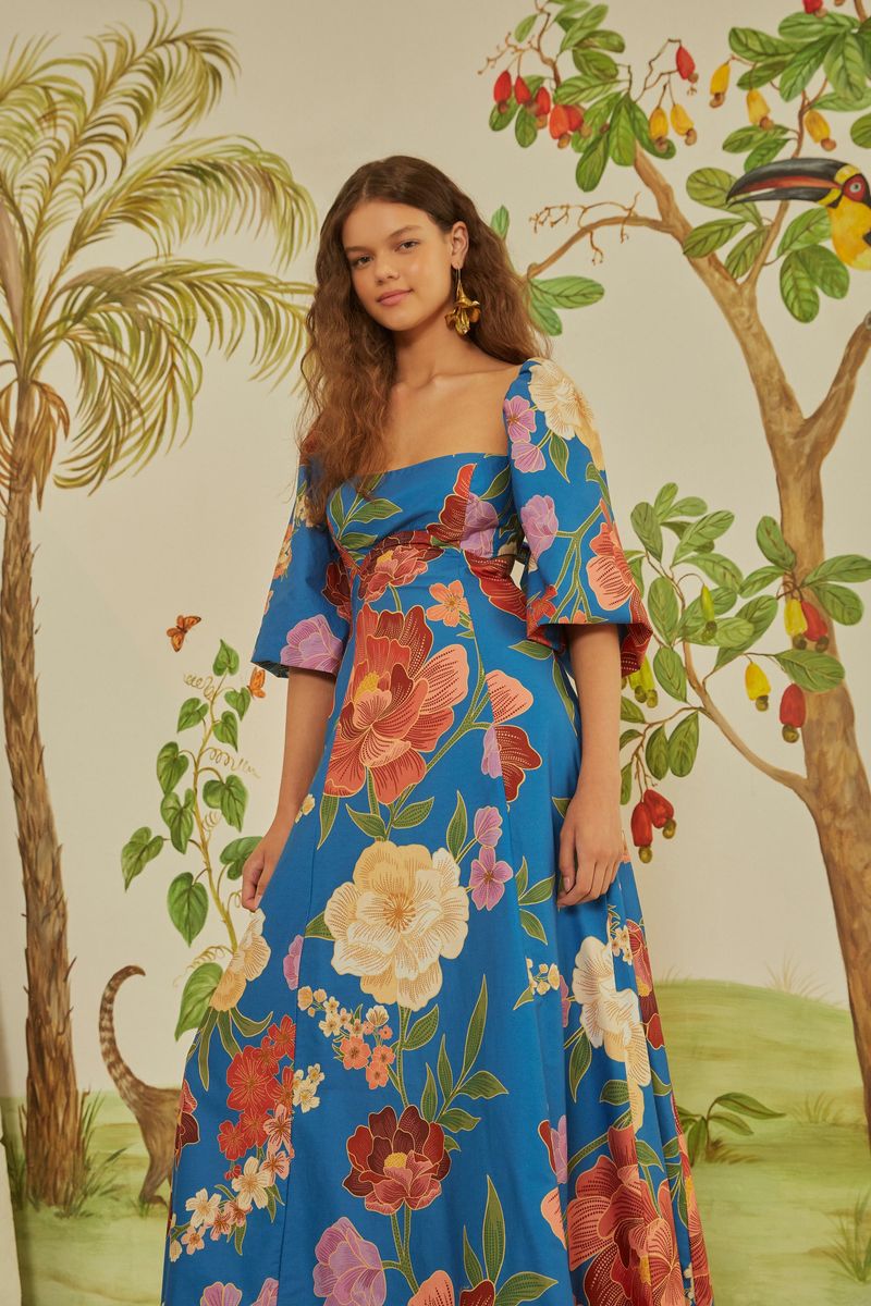 Modelo usando un vestido azul con estampado floral vibrante, en un ambiente tropical.