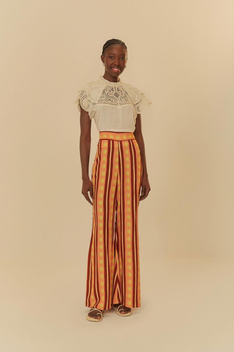 Modelo-usando-pantalon-largo-estampado-con-rayas-verticales-en-tonos-de-naranja-y-rojo-vista-lateral.