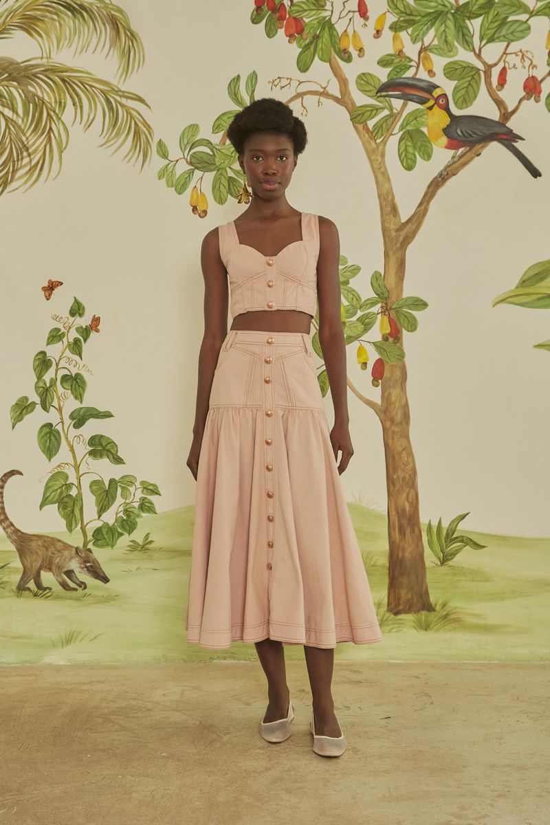Modelo usando falda midi rosa claro con botones frontales en un escenario tropical.