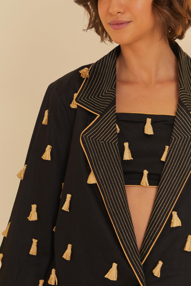 Detalle de la solapa del blazer negro con borlas de rafia.