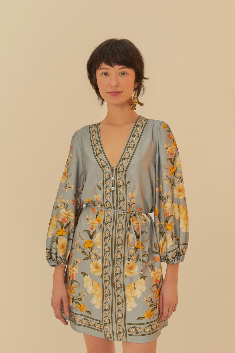 Vestido corto estampado con flores amarillas y detalles verdes, con mangas largas abullonadas y escote en V profundo.