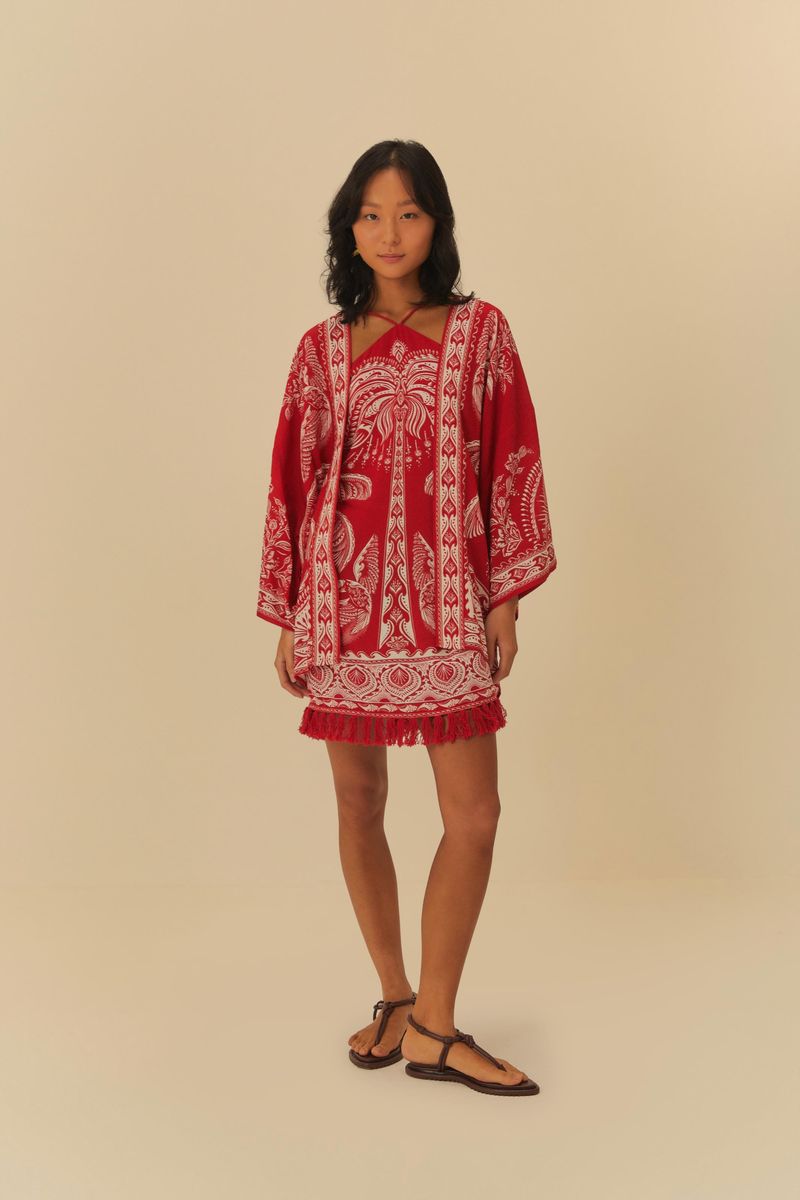 Vestido corto estampado con palmeras sobre fondo rojo, con mangas largas y detalles decorativos.