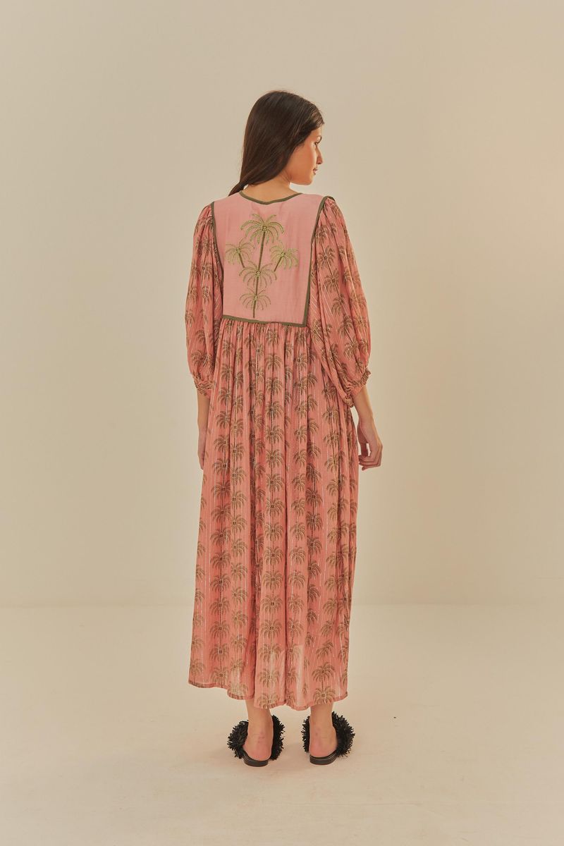 Vista completa del vestido estampado con palmeras, sobre fondo rosa y detalles verdes.