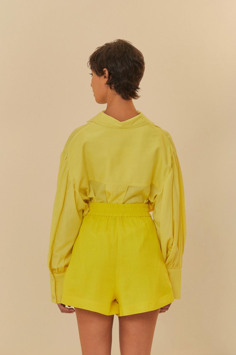 Vista trasera de la modelo llevando el conjunto amarillo, mostrando el ajuste del short en la cintura.