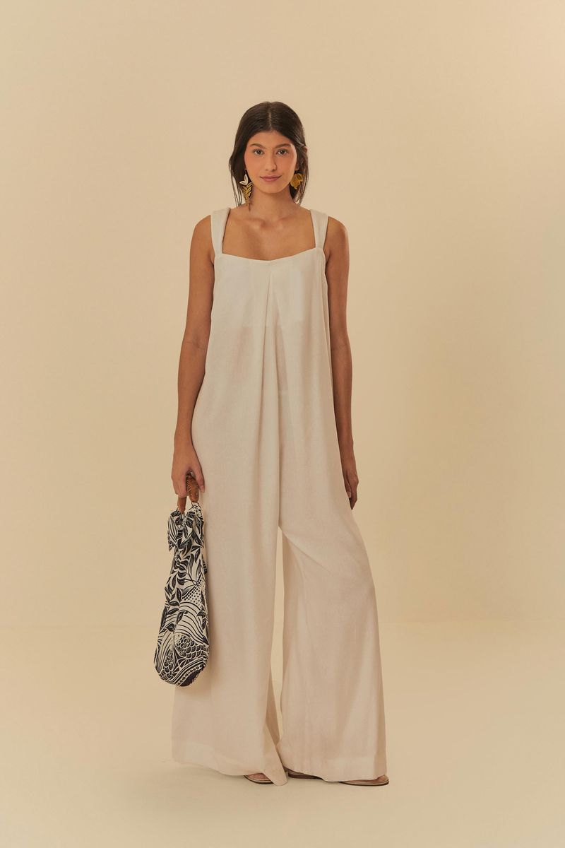 Modelo usando un enterito beige con pliegues frontales, sosteniendo una bolsa estampada.