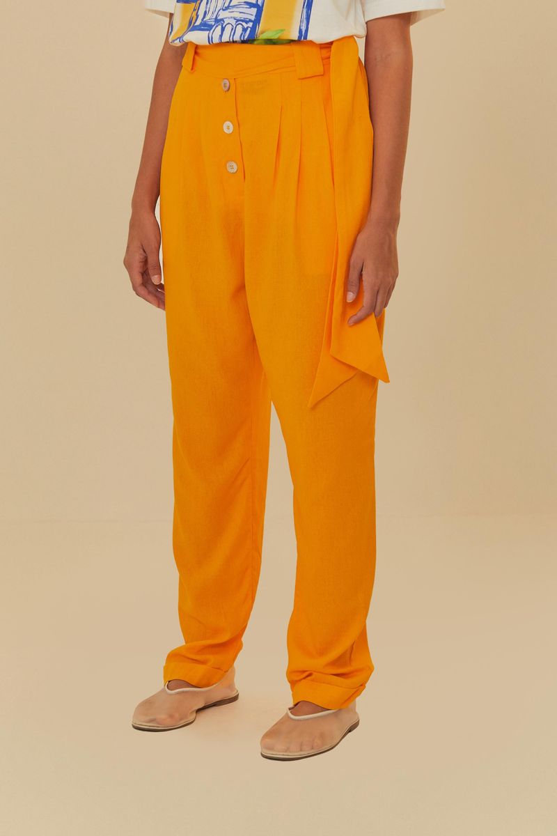 Primer plano de la cintura alta del pantalón naranja, mostrando el detalle de los botones y el bolsillo frontal