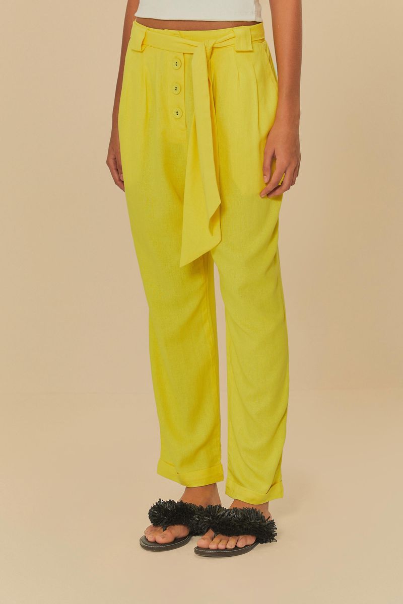 Detalle de la cintura del pantalón amarillo con botones y cinturilla lisa.
