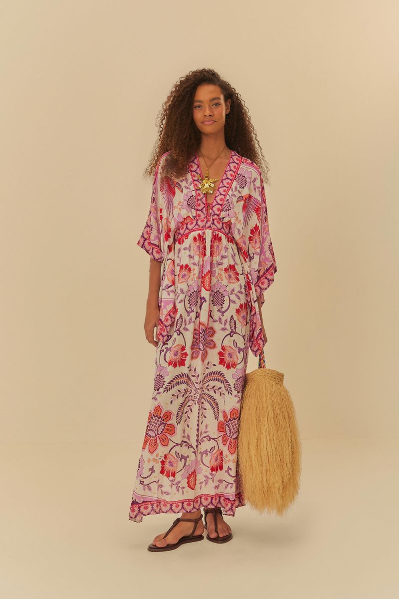 Modelo-usando-vestido-largo-estampado-con-patron-tropical-sosteniendo-un-bolso-de-paja.