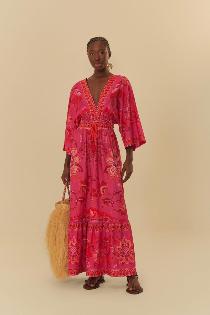 Modelo usando vestido cropped con estampado de tucanes y flores en fondo rosa, sosteniendo una bolsa de yute.