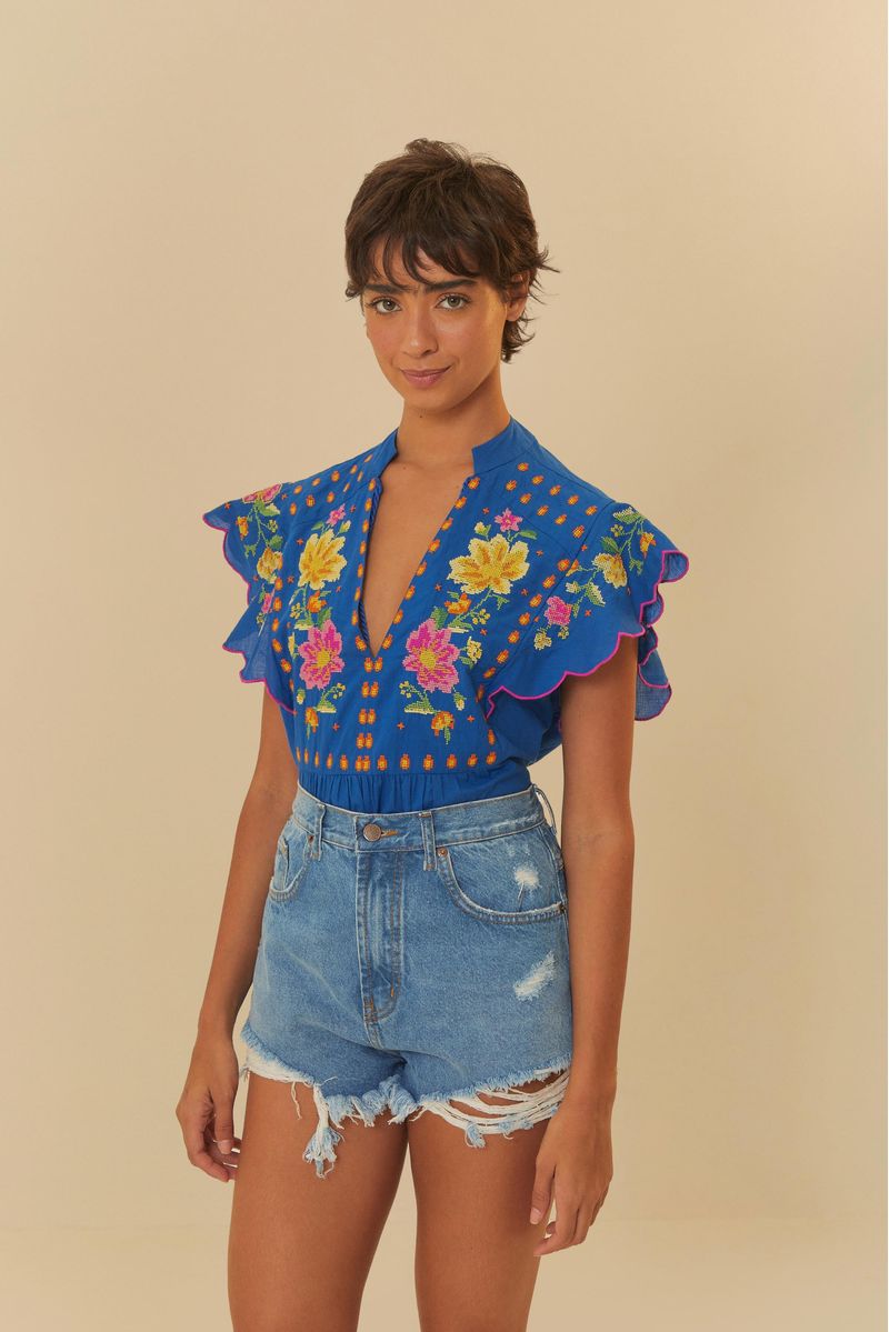 Modelo usando un short de jean azul oscuro con cintura alta y detalles deshilachados, combinado con una blusa azul vibrante con estampado floral.