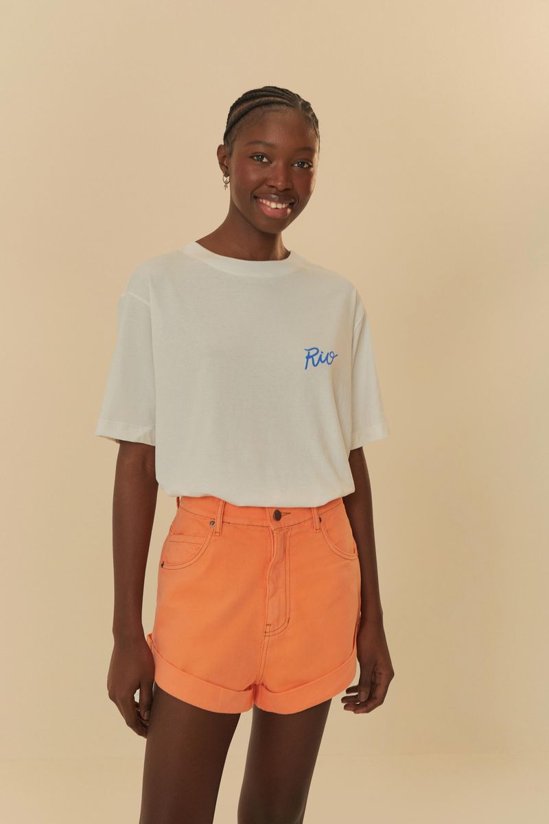 Modelo llevando un short de sarga naranja neón con dobladillo doblado, combinado con una camiseta blanca.