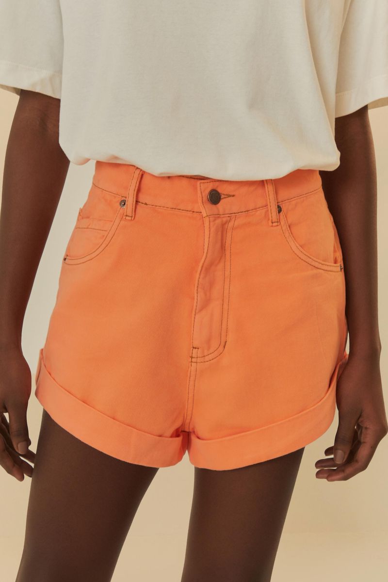 Primer plano del short de sarga naranja neón mostrando detalles del dobladillo plegado y bolsillos frontales.