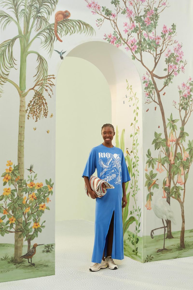 Vestido azul con estampado tropical blanco, longitud cropped y abertura lateral, mostrado en un entorno decorado con motivos naturales.