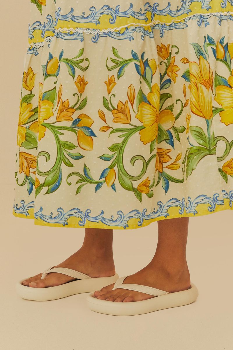 Detalle del vestido largo estampado con flores amarillas y detalles azules, combinado con sandalias.