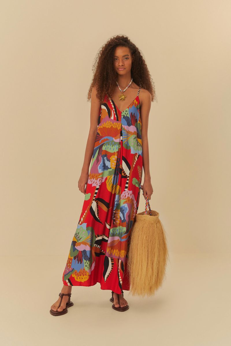 Modelo usando mono floral con tirantes finos y escote en V, sosteniendo una bolsa de paja.