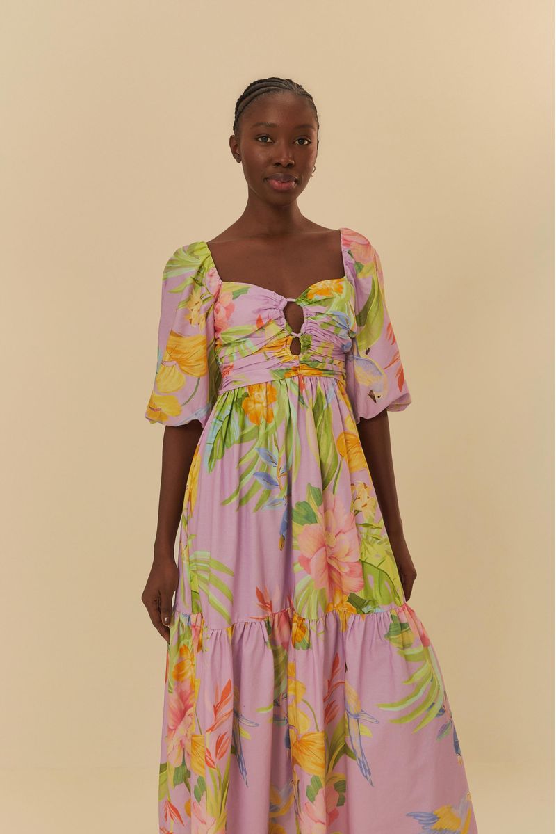 Modelo usando un vestido cropped con estampado tropical sobre un fondo rosa claro, vista frontal.