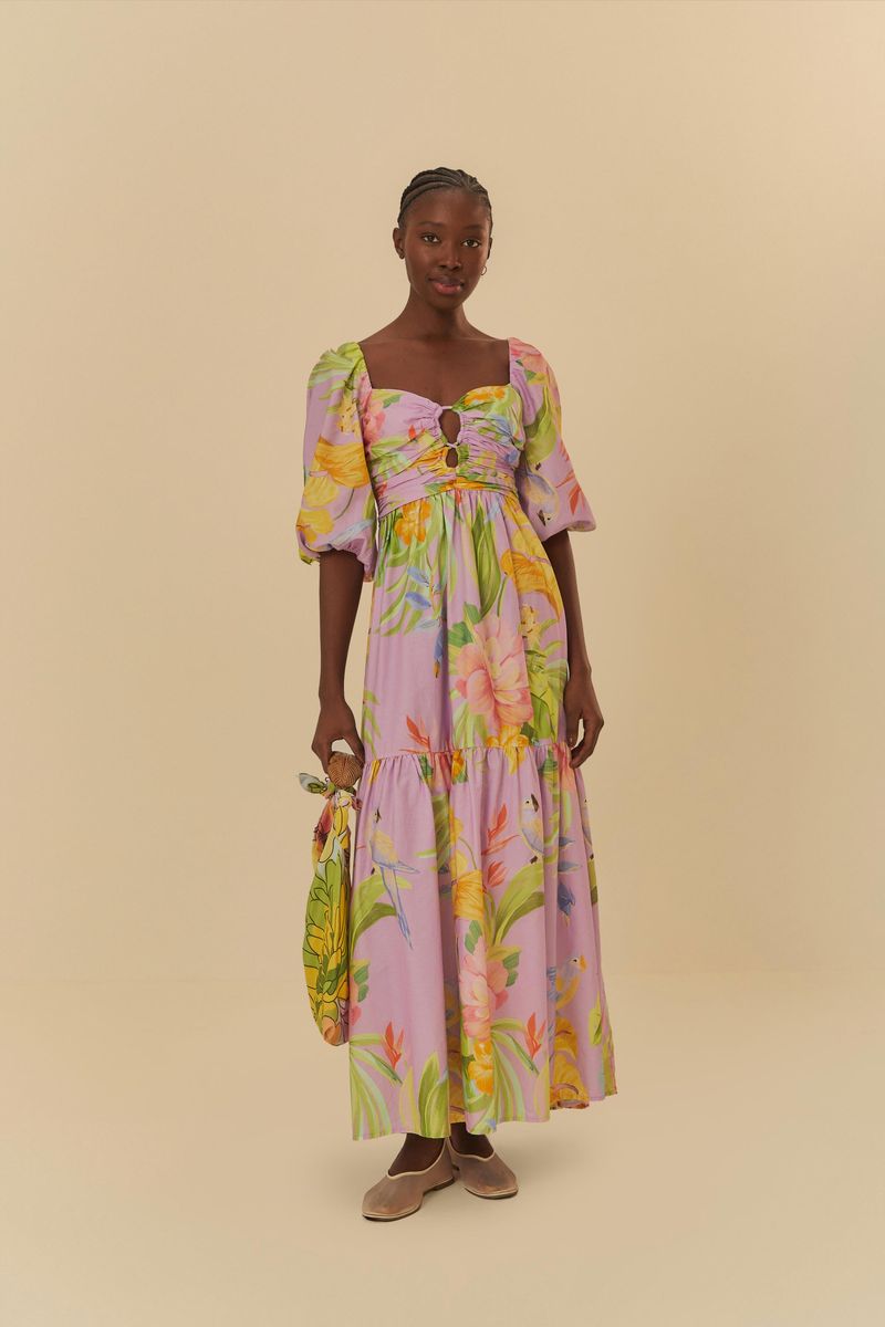 Modelo sosteniendo un bolso, usando un vestido cropped con estampado tropical, vista frontal completa.