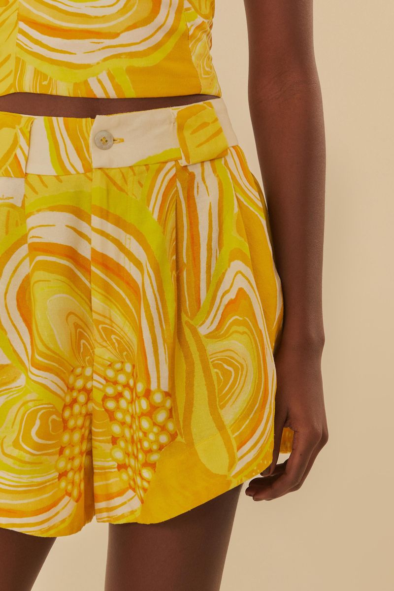 Primer plano del short estampado en amarillo y blanco, destacando el botón y el cinturón.