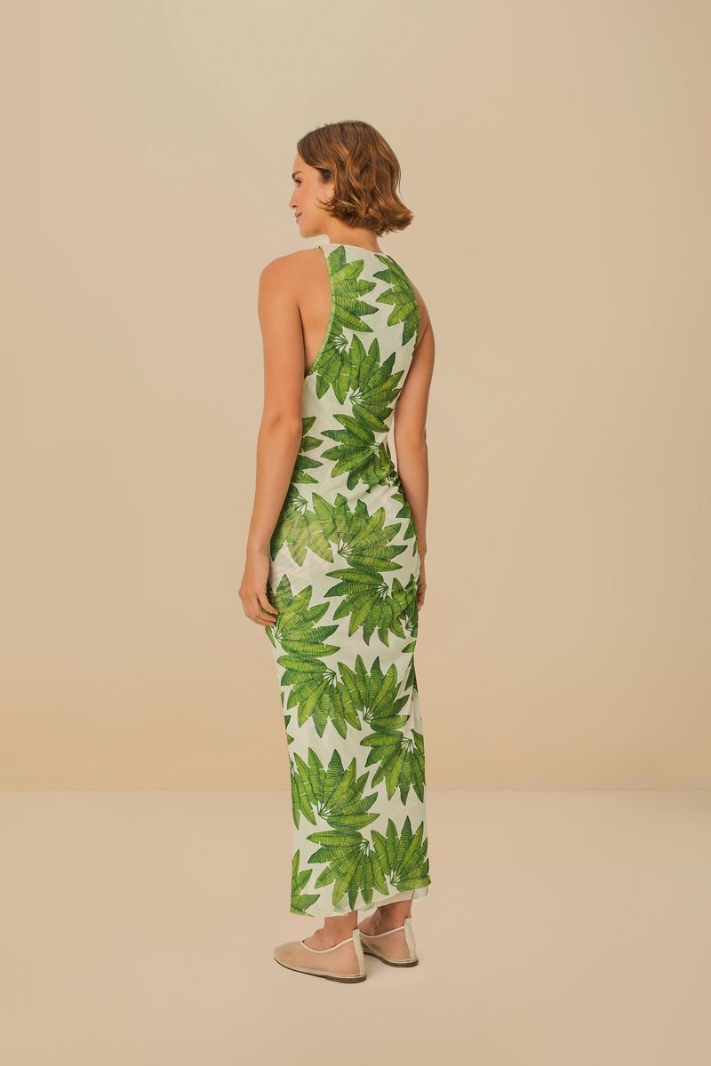 Modelo usando un vestido cropped con estampado de hojas verdes sobre fondo blanco, vista trasera.