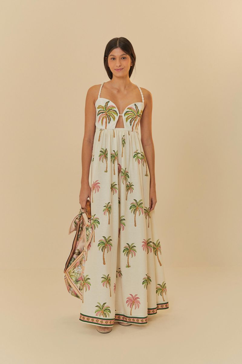 Vestido largo con estampado tropical de palmeras, tirantes delgados y barra decorada, mostrado con un bolso complementario.