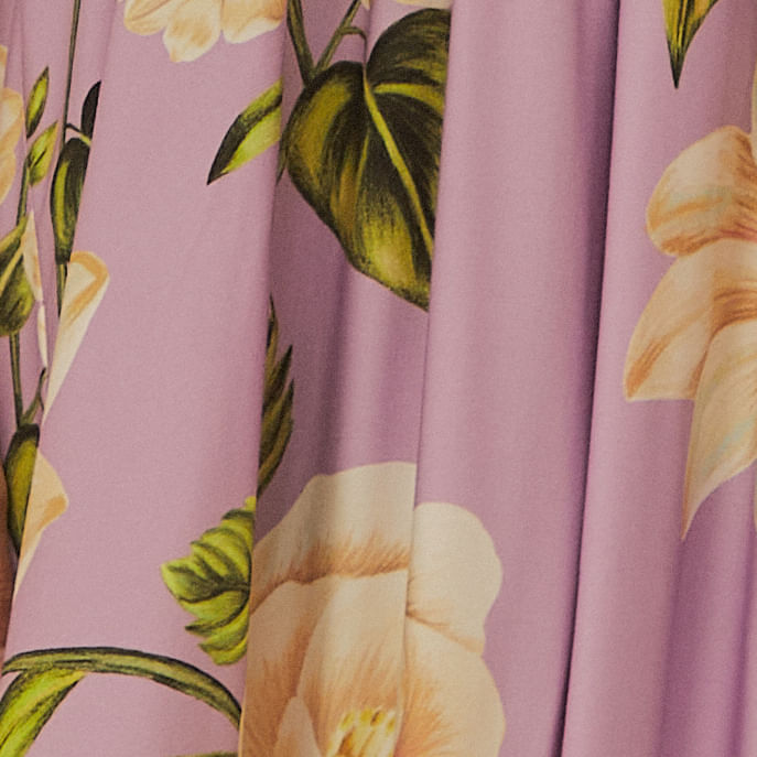 Primer plano del estampado floral del vestido con fondo lila, destacando flores blancas y hojas verdes.