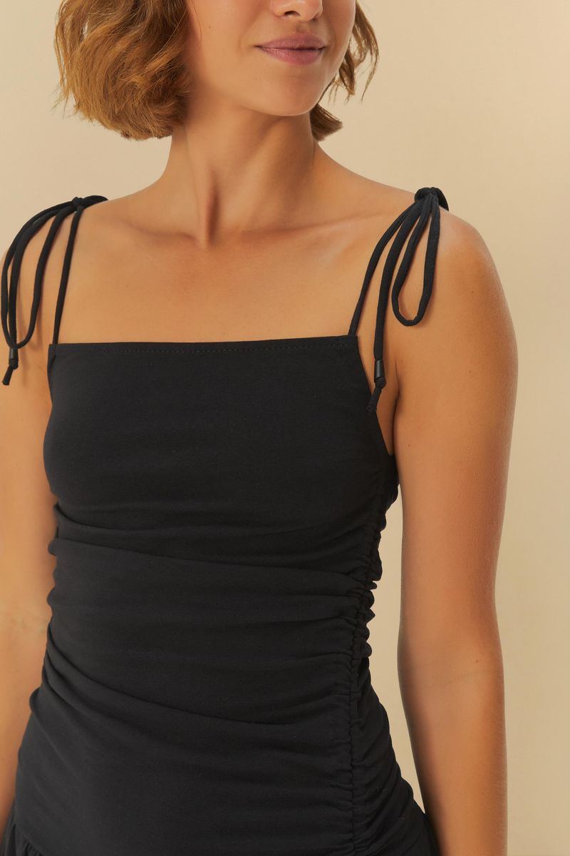 Imagen de un vestido negro con tirantes ajustables y diseño fruncido, mostrando la parte inferior.