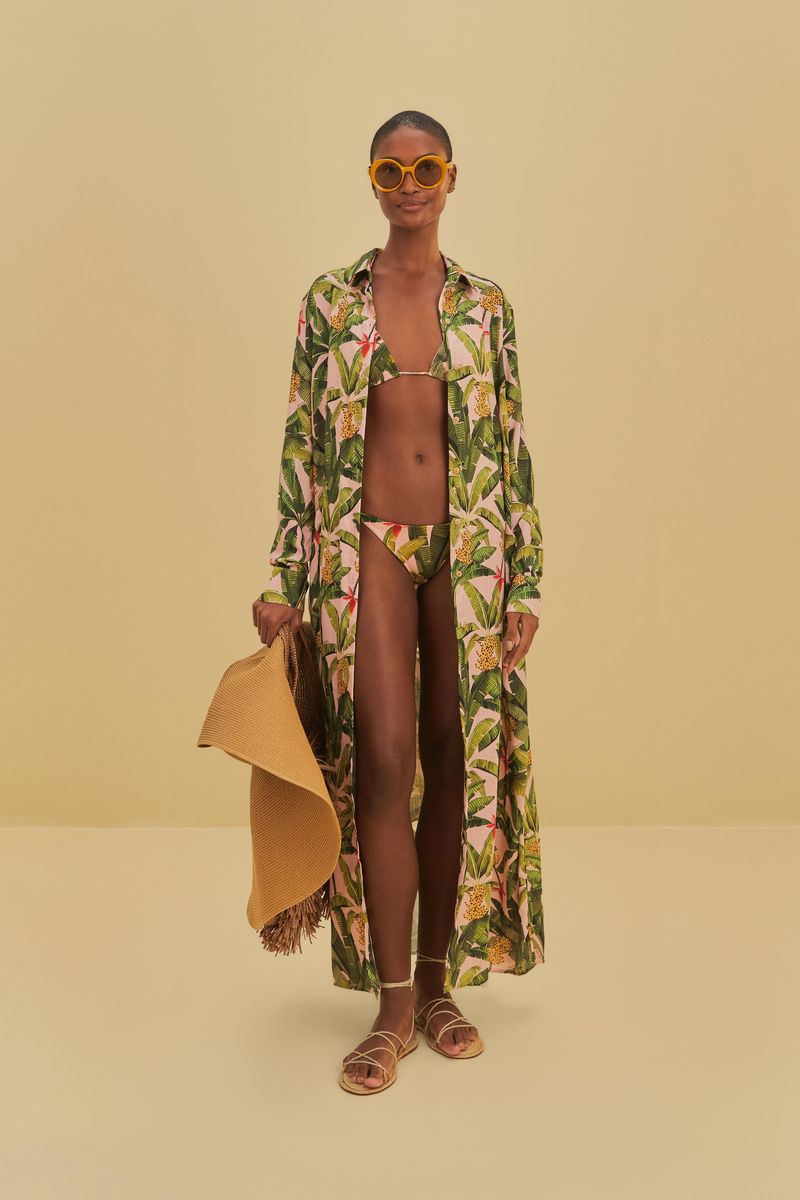 Imagen de una modelo vistiendo un vestido chemise largo con estampado tropical de plátanos y hojas verdes, sosteniendo un sombrero de paja.