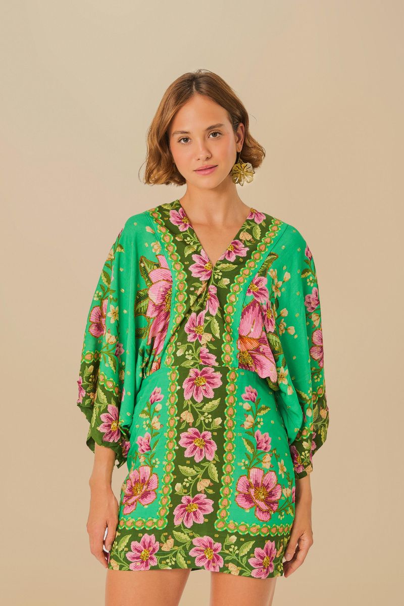 Vestido corto con mangas estilo kimono, estampado floral vibrante sobre fondo verde, vista frontal.