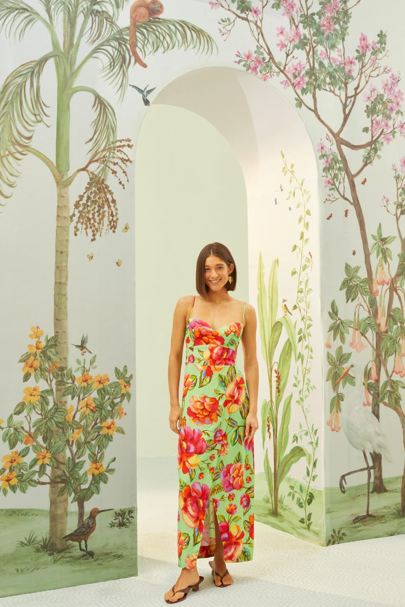 Vestido midi con estampado floral vibrante en un fondo verde claro, tirantes finos y escote en V, mostrado en un entorno decorado con motivos botánicos.