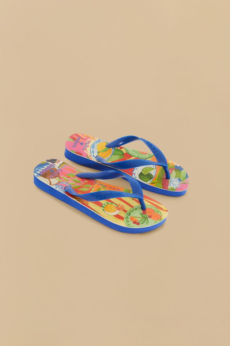 Primer plano de las chanclas Havaianas Picnic mostrando un estampado tropical vibrante con tiras azules sobre un fondo beige