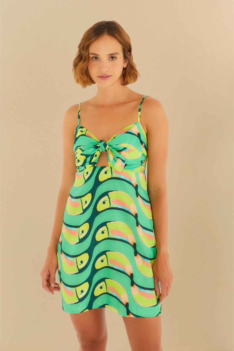 Vestido corto con estampado de tucanes en tonos verde y amarillo, tirantes finos y detalle de nudo frontal.