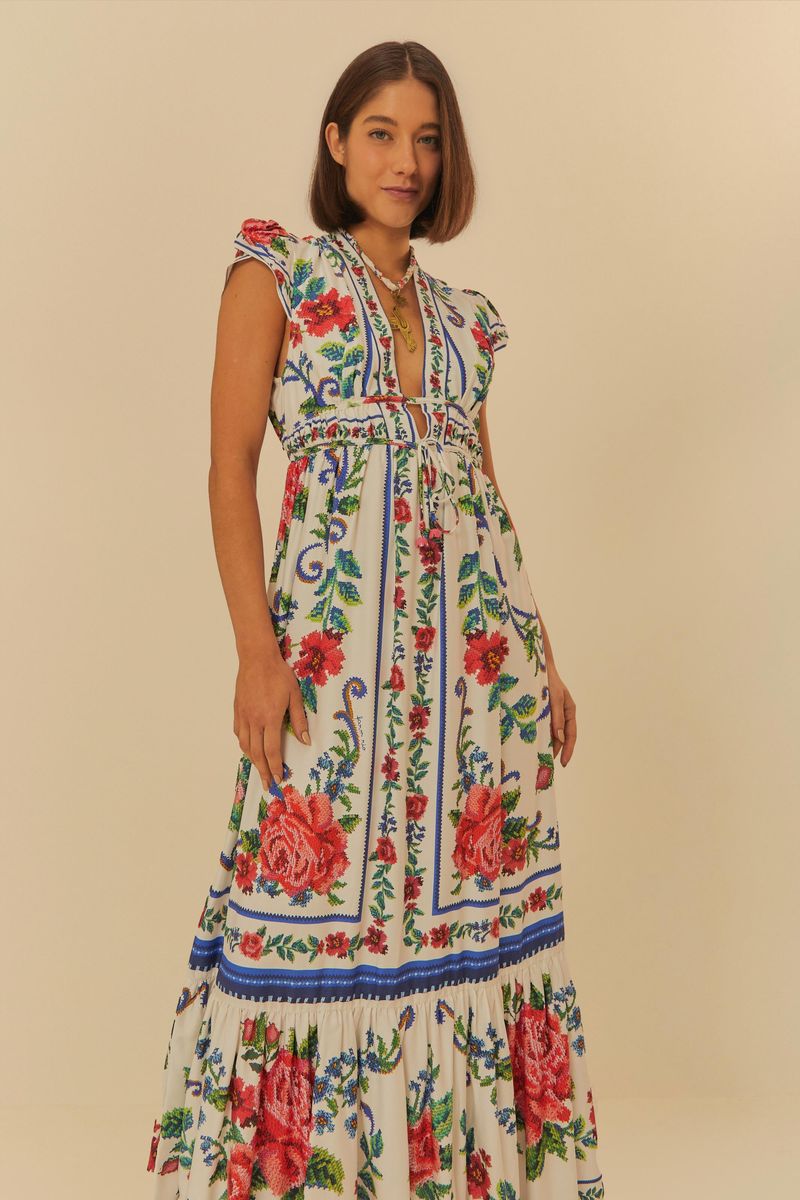 Vestido largo con estampado floral sobre fondo claro, detalles de volantes en el borde inferior y escote en V.