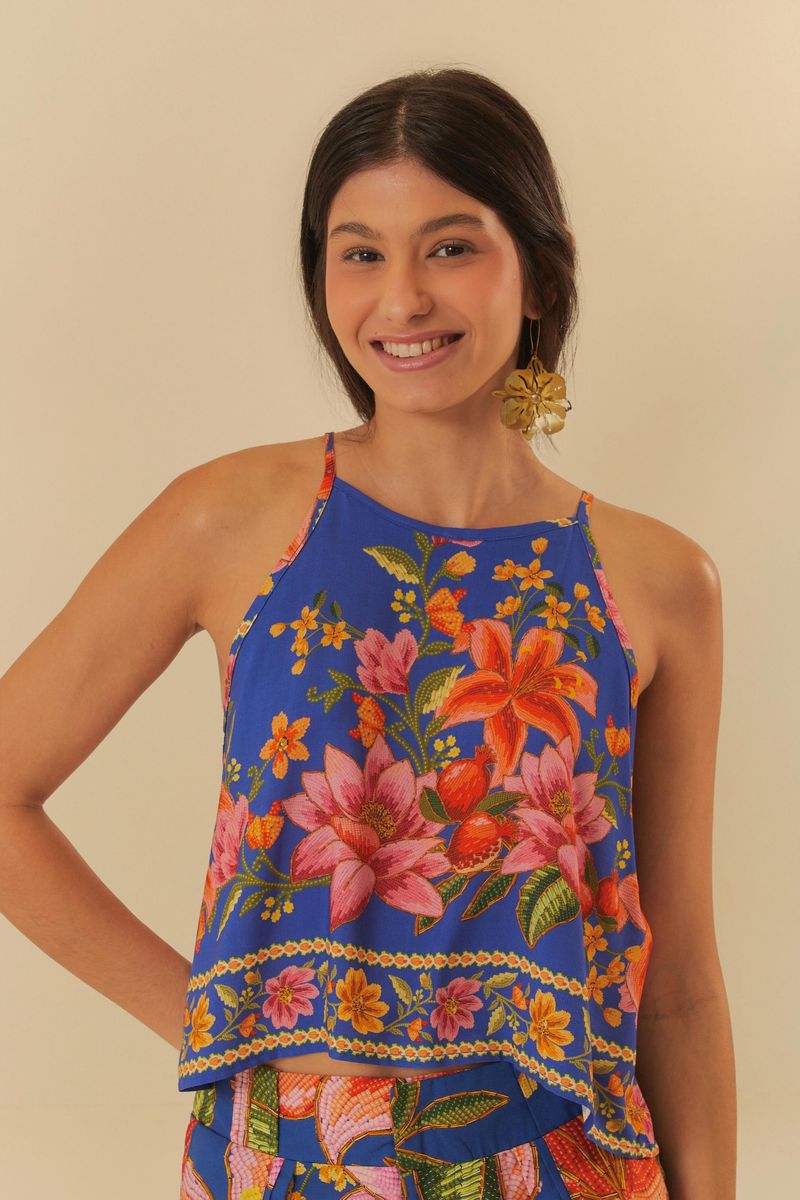 Musculosa estampada con flores tropicales y follaje en fondo azul, vista frontal.