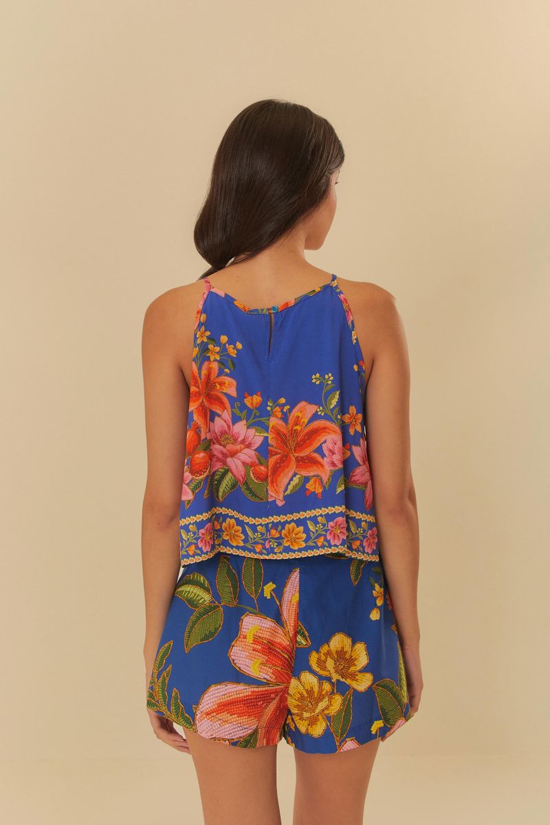 Musculosa estampada con flores tropicales y follaje en fondo azul, detalle del tejido.