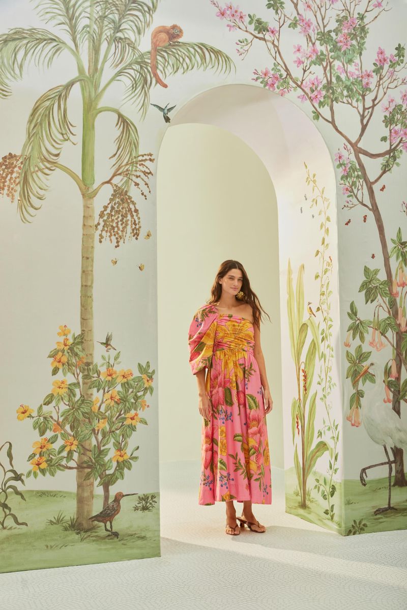 Vestido estampado con diseño tropical en fondo rosado, exhibido en un entorno decorado con elementos naturales.