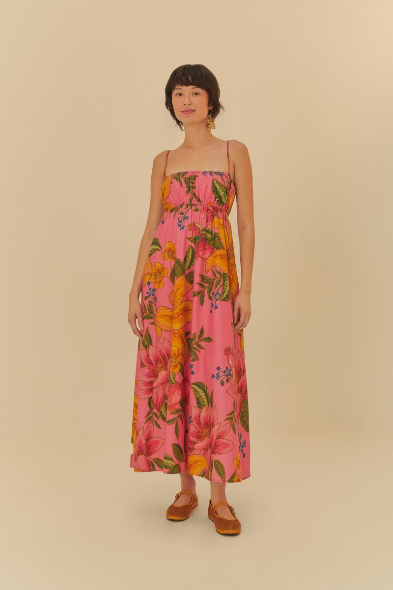 Vestido largo con estampado y tirantes finos, fondo rosado y detalles de frutas y flores vibrantes.